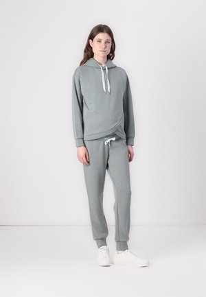 Hoodie harma, pehmeä kangas, jossa on ylöspäin risteävä muotoilu ja vaaleanvihreät nyörit, yhdistettynä yhteensopiviin collegehousuihin. Valkoiset lenkkarit täydentävät asun.