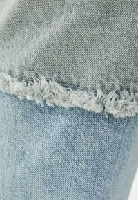 Tela de mezclilla azul claro con un detalle de dobladillo deshilachado en la parte inferior. La textura parece ligeramente desgastada, mostrando un diseño casual.