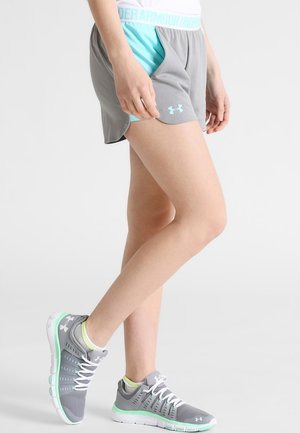 Person iført grå og turkis Under Armour-shorts og grå atletiksko med mintgrønne accenter på hvid baggrund.