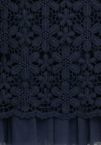 Dunkelblauer Spitzenstoff mit komplexen Floralmustern und strukturierten Details, mit einem gefalteten unteren Abschnitt und gewellten Kanten.