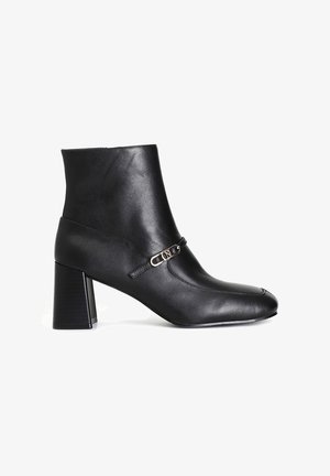 Stivaletto in pelle nera con punta quadrata, tacco a blocco e una fascia decorativa con dettaglio della fibbia in tono oro. Texture liscia.