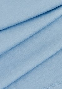 Világoskék pamut szövet, gondosan összehajtva, sima felülettel és diszkrét bordázattal, tiszta szélekkel és látható minták vagy fémrészletek nélkül.