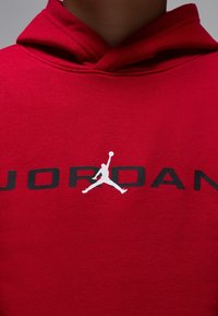 Red hoodie made of soft fabric features a front kangaroo pocket, large "JORDAN" text in black, and a white Jumpman logo.