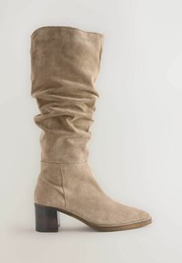 Beige suède laarzen tot de knie met een gerimpeld ontwerp, vierkante neus en een chunky houten hak. Gladde textuur met subtiele stikseldetails.