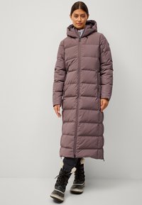 Cappotto lungo e voluminoso in lavanda tenue con cappuccio, dotato di sezioni trapuntate e chiusura frontale con zip. Abbinato a stivali neri isolati.