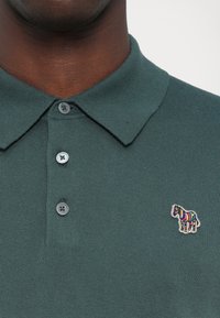 Polo shirt in donkergroen met een geribbeld textuur, voorzien van drie knopen en een kleurrijk, geborduurd zebraontwerp op de linkerkant van de borst.