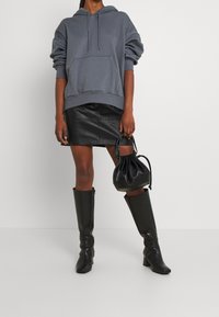 Grå hoodie med framficka, svart läder minikjol, knähöga svarta stövlar och en liten svart dragsko-handväska. Släta texturer och avslappnad passform.