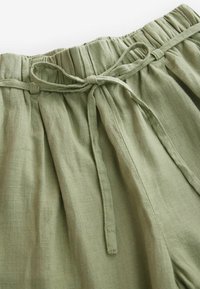 Pantaloni in misto lino verde chiaro con vita arricciata, lacci regolabili e texture morbida. Presentano pieghe per un tocco di stile e comfort.