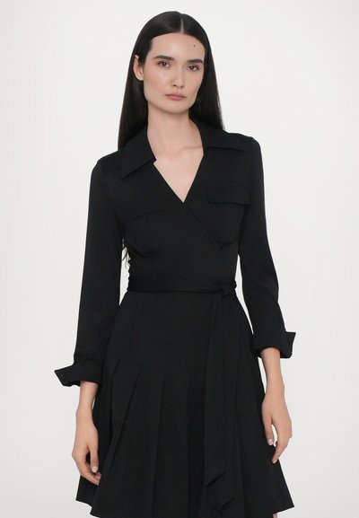 Čierne zavinovacie šaty s dlhými rukávmi, golierom, zapínaním na gombíky na manžetách, dvojitými náprsnými vreckami a viazaním v páse. Skladaná sukňa zabezpečuje plynulý pohyb.