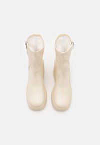 Paire de bottes crème mi-mollet avec fermetures éclair latérales, bouts arrondis et semelles épaisses, vues de dessus sur un fond uni.