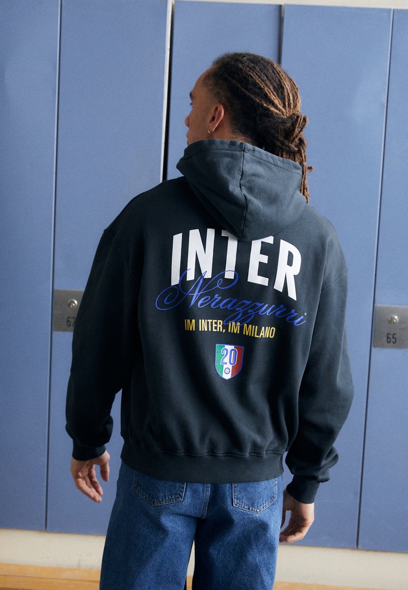 Hoodie preto com texto branco e azul "INTER" e "Nerazzurri" nas costas. Apresenta um emblema colorido e "20" num pequeno design.