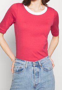 Top rosso a maniche corte con scollo rotondo bianco; design aderente; realizzato in tessuto leggero e morbido; abbinato a jeans blu a vita alta.