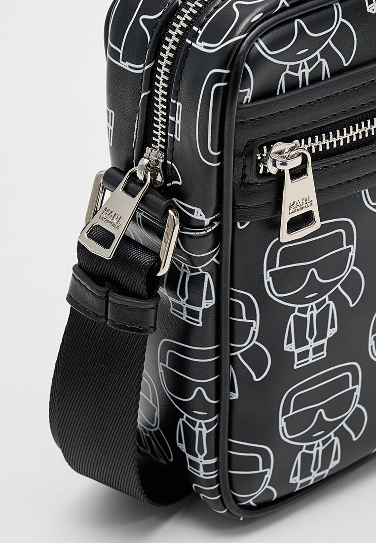 Bolso sintético negro con un patrón de dibujos animados blancos, cierre de cremallera, herrajes plateados y una correa ajustable desmontable.