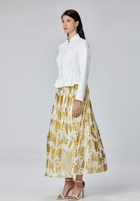 Veste blanche à boutons, ajustée avec un ourlet peplum, associée à une longue jupe à motifs floraux jaunes et blancs. Complétée par des talons blancs à lanières.