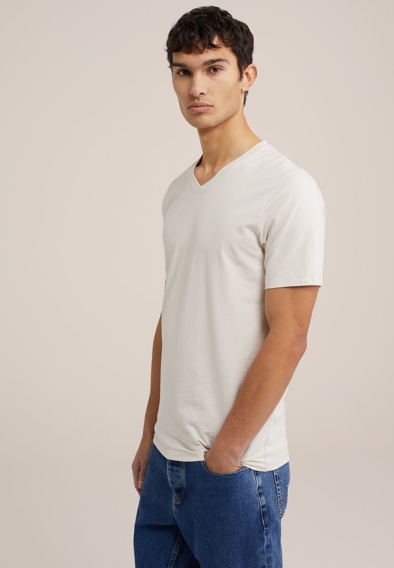 V-veida, īsām piedurknēm T-krekls gaiši beigetā krāsā, izgatavots no mīkstas auduma ar gludu tekstūru, kombinēts ar ziliem džinsu biksēm.