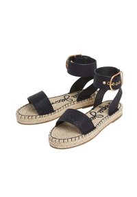 Juodos espadrilės su dviem plačiomis petnešomis ir sagtimi, turinčios nertas džuto padą ir tekstūruotą pėdos dalį su iškiliais detalėmis.