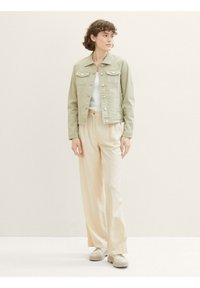 Hellgrüne Jeansjacke mit zwei Vordertaschen, Knopfverschluss und cropped Design. Kombiniert mit crèmefarbenen Schlaghosen und Sneakers.