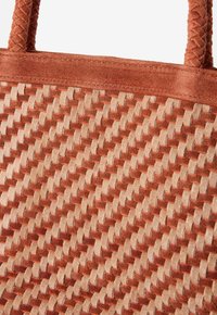 Sac en daim avec des poignées tressées et un motif texturé tissé dans des couleurs alternées de rouille et de beige.