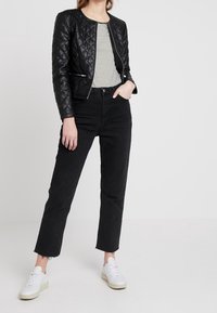 Veste en cuir noir matelassé, haut rayé, jeans noirs taille haute, ourlet effiloché, baskets blanches ; design minimaliste avec une coupe cintrée.