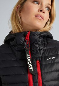 Sort pufferjakke med en rød lynlås og detaljer, der har hætte, quiltet tekstur og mærketag med teksten "JACK1T."