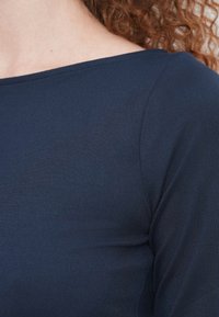 Μπλε ναυτικό, εφαρμοστό μπλουζάκι με μακριά μανίκια από λείο ύφασμα, με φαρδύ ντεκολτέ σε σχήμα βαρκούλας και διακριτικές ραφές.