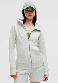 Lys grå zip-up hoodie med hætte, lange ærmer, frontlommer og en tætsiddende design, parret med matchende shorts. Materiale i bomuldsblanding.