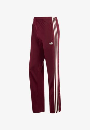 Calças desportivas de cor bordô feitas em tecido macio, com três riscas brancas ao longo dos lados e um bolso com fecho na perna esquerda.