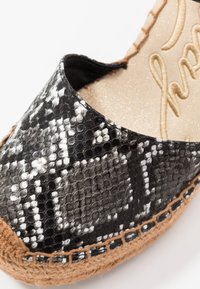 Černobílá texturovaná espadrilka se vzorem hadí kůže, s pletenou jútovou podrážkou a lesklým černým svrchním materiálem.