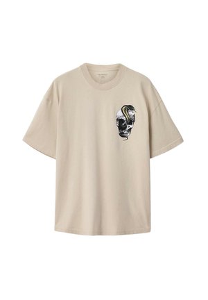 Beigenvärinen puuvillainen t-paita, jossa on löysä istuvuus ja vasemmassa rintakehässä kallokuvio, jota korostaa vihreä käärme. Lyhyet hihat.