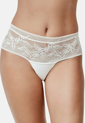 Witte kanten lingerie met bloemenborduursel, gedragen op de heupen, die het midden van de buik en de bovenbenen toont van een persoon met een lichte huid.