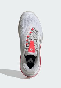 Zapatilla deportiva blanca con parte superior de malla, cordones grises, un acento rosa brillante en la lengüeta y el talón, y una suela estampada para tracción.