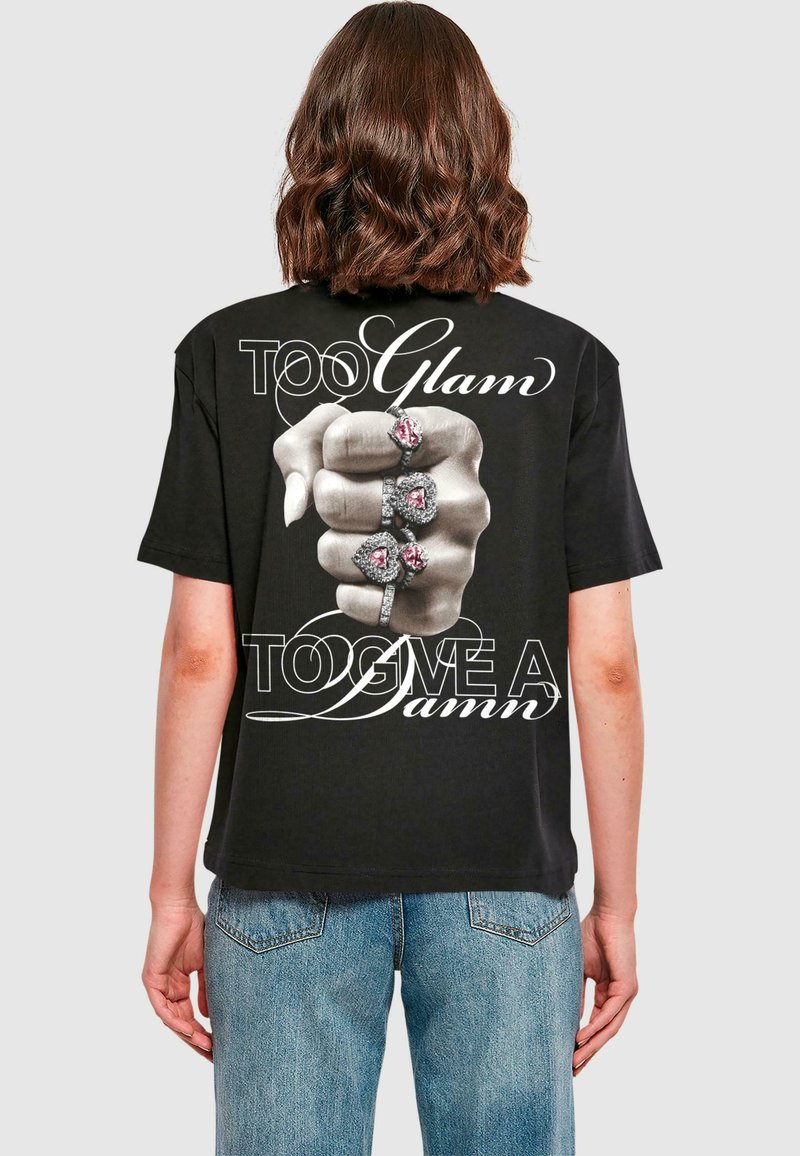 Black cotton t-shirt featuring a graphic of a hand with rings. Text reads "TOO Glam" and "TOO GIVE A Damn" in white cursive lettering.