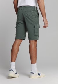 Olijfgroene cargoshorts met meerdere zakken, riemlussen en een rechte snit. Gecombineerd met witte sokken en lichte sneakers.