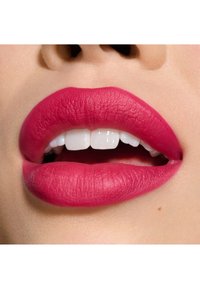 Matt hot pink leppestift på glatte, fyldige lepper med synlige hvite tenner og en myk, naturlig hudtone; minimal tekstur og ingen glans.