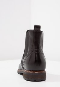 Stivaletto in pelle nera con punta rotonda, pannelli laterali elasticizzati, dettagli decorativi a brogue e tacco impilato marrone.