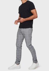 Maglietta nera di cotone, pantaloni slim-fit a quadri grigi e sneaker bianche. I pantaloni presentano un motivo a scacchi e una texture sottile.