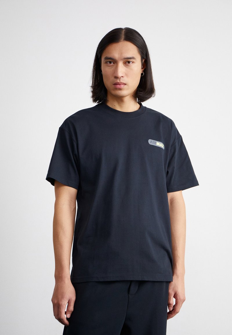 Schwarzes T-Shirt mit kurzen Ärmeln aus Baumwolle. Es hat einen runden Halsausschnitt und ein kleines "AIRMAX"-Logo in grün und weiß auf der linken Brust.