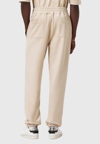 Beige joggebukser med elastisk talje og to baglommer. Med ribkant ved anklerne og parret med hvide sneakers med sorte og slangeskindsdetaljer.