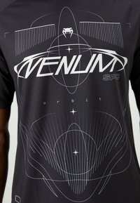 T-shirt graphique noir avec des motifs géométriques blancs, texte "VENUM SPC" et un logo de serpent. Fabriqué en tissu léger et respirant.