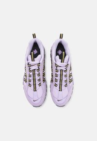 Lila nät-sneakers har svarta och gyllene randiga accenter, texturerade sulor och en distinkt snörningsdesign med en logotyp på sidan.