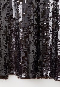 Tela de lentejuelas negras con lentejuelas circulares en tonos variados de gris y plata, creando una superficie texturizada con un acabado reflectante.