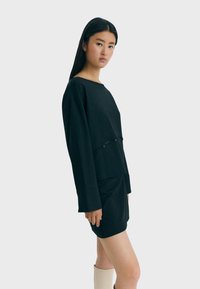 Schwarzes Sweatshirt und Rock-Set; weicher Stoff, lockere Passform, lange Ärmel. Enthält Knopfakzente und ein kurzes Design. Schlichter, moderner Stil.