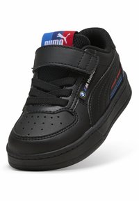 Baskets synthétiques noires avec un bout rond, fermeture à lacets et Velcro, tige texturée, et accents notables en bleu et rouge.