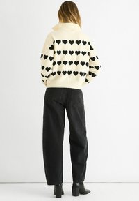 Cream sweater with black heart patterns, high collar, and ribbed hem, paired with black wide-leg pants and heeled ankle boots.