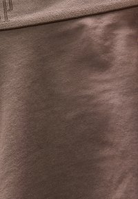 Tissu marron avec une ceinture texturée et un matériau en tricot lisse, présentant des plis subtils et des détails de couture.