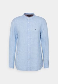 Chemise à manches longues bleu clair en lin, avec un col montant et une fermeture à boutons sur le devant. Petit logo sur la poitrine.