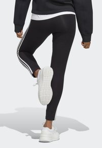 Sorte leggings med hvide sidelister, fremstillet af et glat stof, parret med hvide atletiske sko med en tekstureret sål.