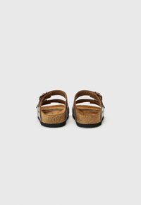 Brune lærslippers med korksåle med en teksturert overflate, justerbar reim med metallspenne og åpen bakdesign.