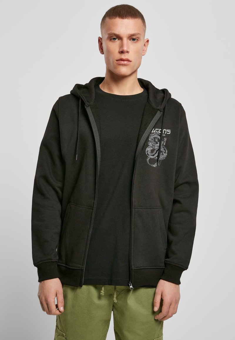 Black zip-up hoodie featuring a front pocket and graphic design on the chest, worn over a black t-shirt, paired with green cargo pants.