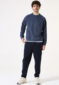 Donkerblauwe sweatshirt met een ronde hals en raglanmouwen, gecombineerd met donkerblauwe joggingbroek. Beide hebben een casual, gestructureerde stof.
